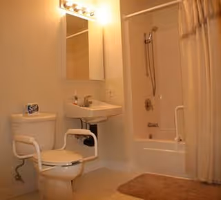Accessible bathroom with a toilet fitted with grab bars, a pedestal sink under a mirrored medicine cabinet, and a bathtub with shower and curtain.
