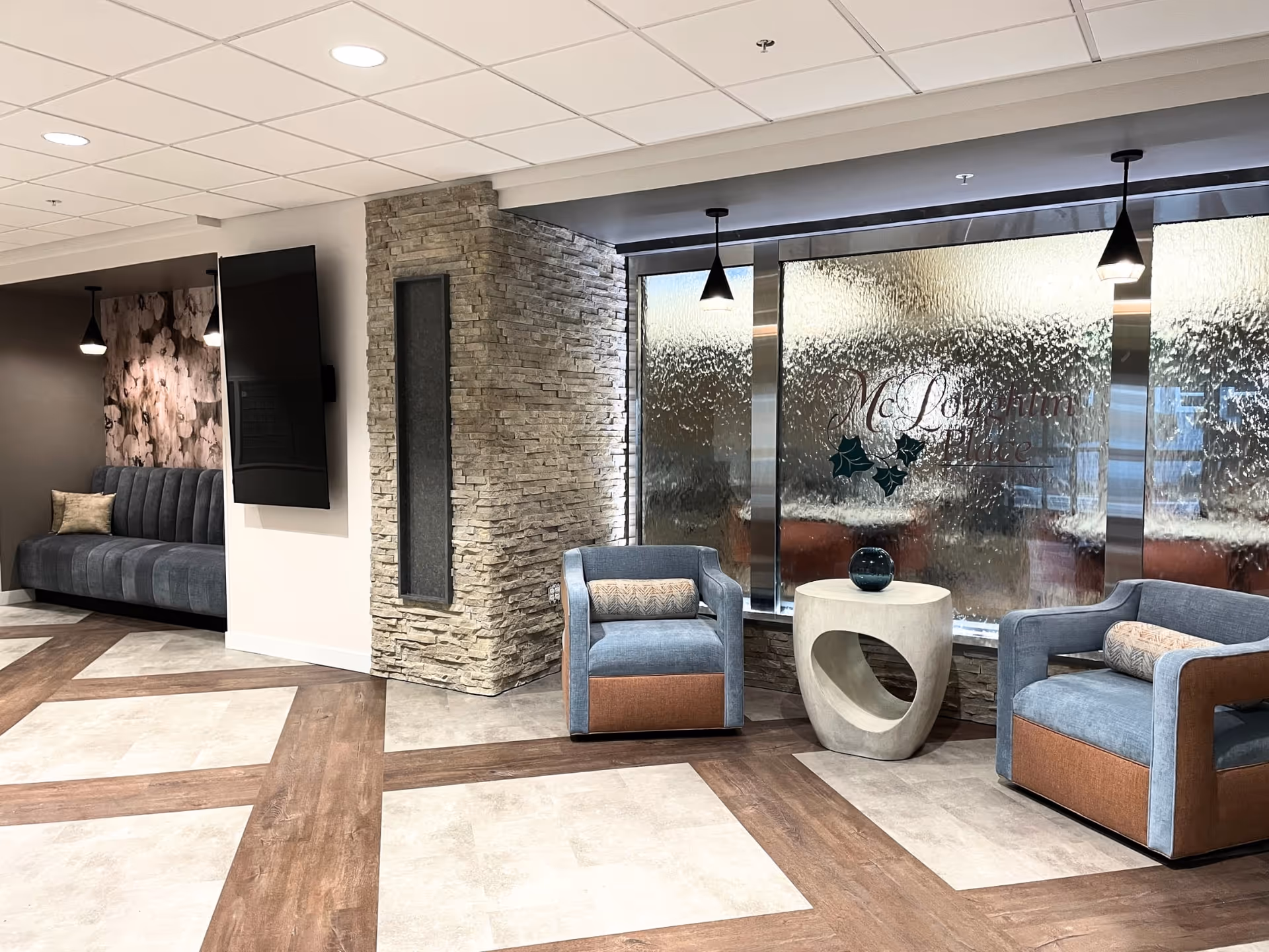 Modern lobby seating area with blue chairs, stone pillar, frosted glass wall signage.