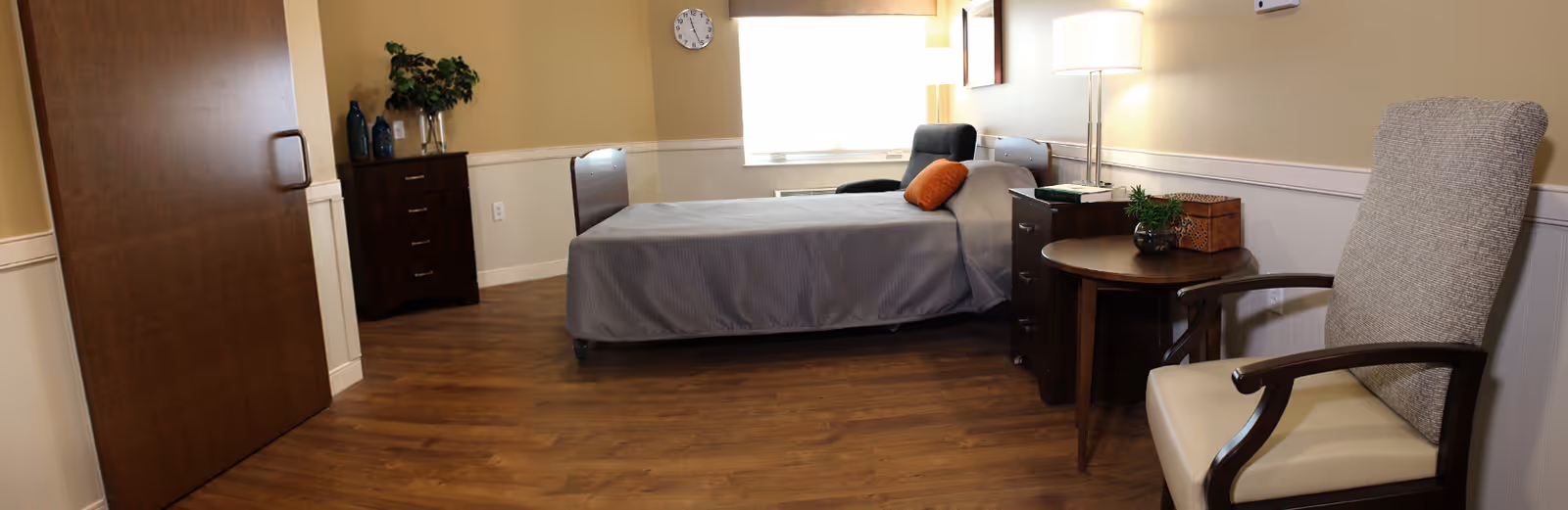A clean, well-lit single resident bedroom with a bed, nightstands, armchair, dresser, and hardwood floor.