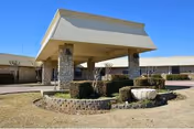 Front entrance of a single-story building with a large canopy, stone columns, and circular landscaped island.