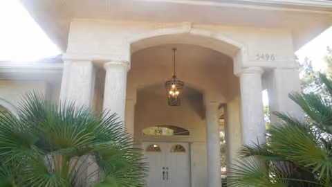 Front entrance of Angels House Adult Care with arches, columns, hanging lantern, and palm plants.