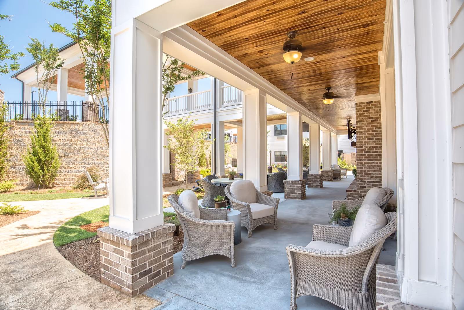 Covered outdoor patio with wicker seating and columns beneath a wooden ceiling.