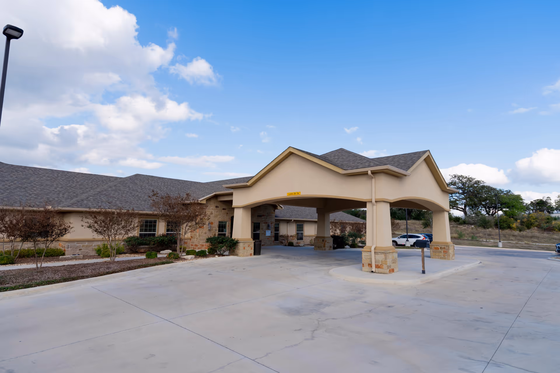 Exterior view of a beige senior living facility with a covered drive-through entrance and wide concrete driveway.