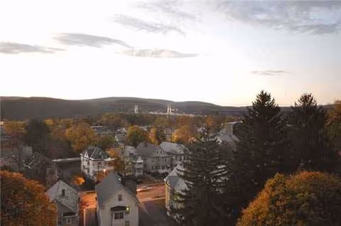 Sunset over a tree-lined neighborhood with houses and distant hills.