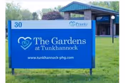 Outdoor view of a blue sign for The Gardens at Tunkhannock, located at 30, with a building and greenery in the background.