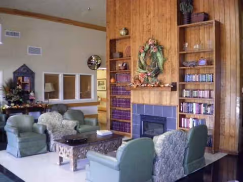Cozy senior living lounge with fireplace, wreath, and green upholstered seating.