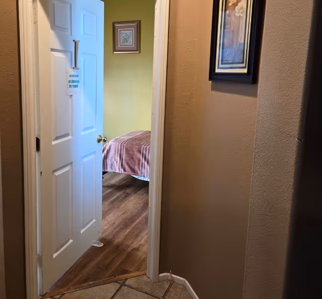 Open doorway reveals a bedroom with a bed and framed art along olive-green walls.
