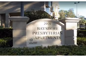 Stone sign reading Bayshore Presbyterian Apartments at the entrance with landscaping.