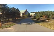 Driveway leading to a brick senior living facility building surrounded by trees and lawns under a clear sky.