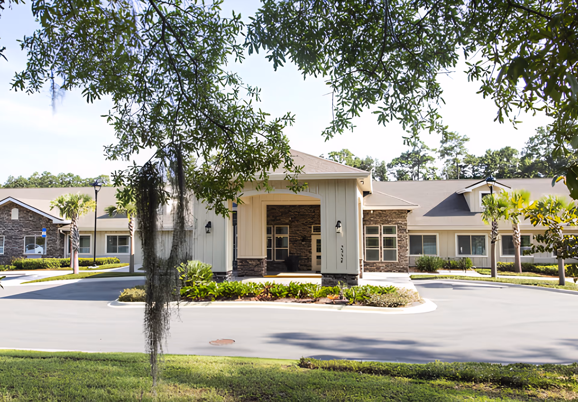 Front exterior view of Azalea Gardens Assisted Living & Memory Care building with a covered entrance, surrounded by greenery and trees.