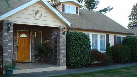 Front exterior of Lia's Elder Care Home with wooden door and trimmed shrubs.
