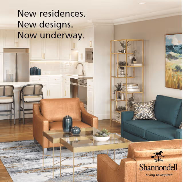 A modern open-concept living room and kitchen area featuring a teal sofa with patterned pillows, two brown armchairs, a glass coffee table with decorative items, a gold shelving unit with plants and books, and a white kitchen with stainless steel appliances and a breakfast bar with two chairs. Text on the image reads 'New residences. New designs. Now underway.'