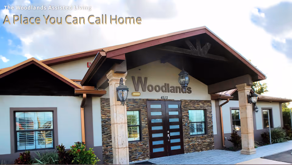Front entrance of The Woodlands Assisted Living building with a covered entry, double doors, and signage.
