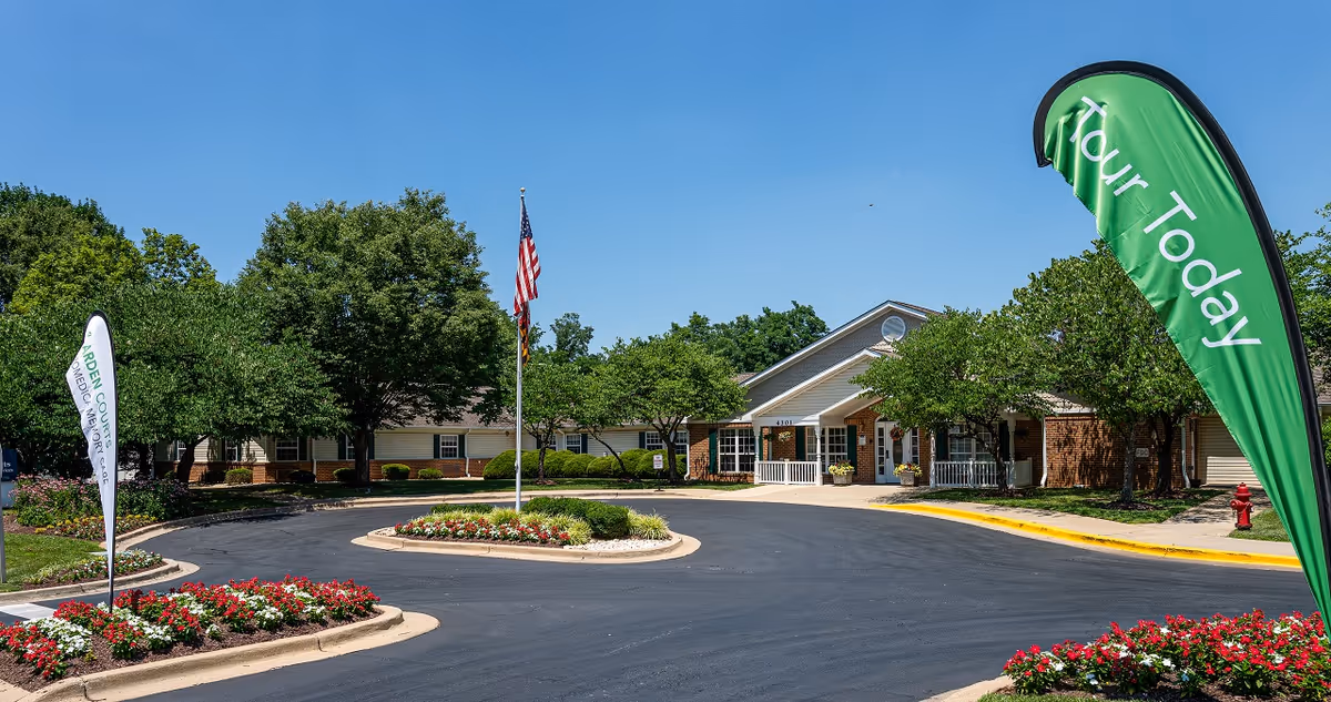 Exterior view of Arden Courts Kensington, entrance with flag, circular driveway and landscaped flower beds.