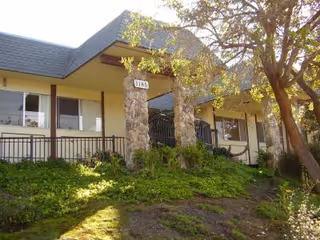 Front view of a single-story senior living facility with a ramp and greenery.