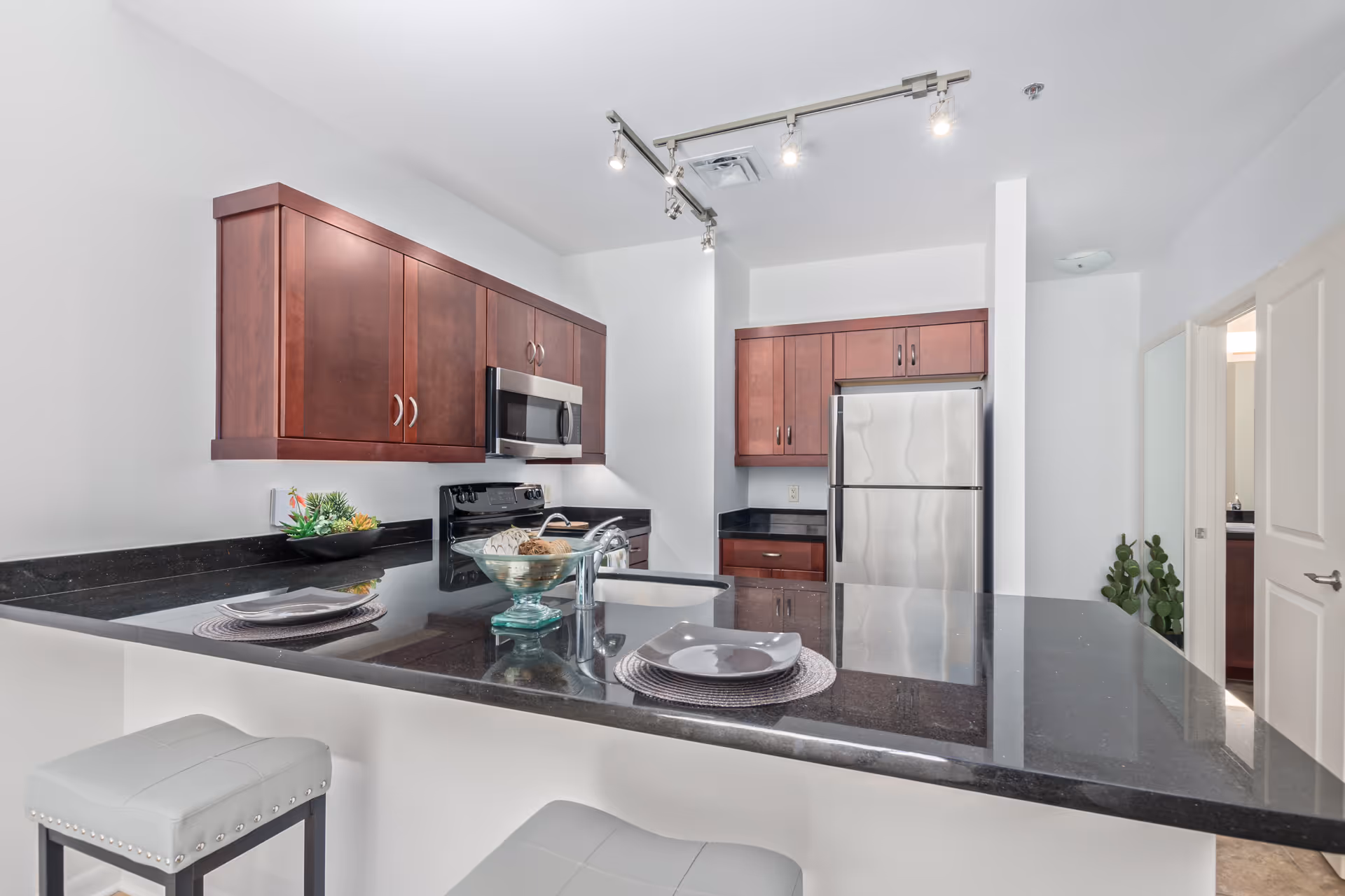 Modern kitchen with a dark granite island and bar stools, cherry wood cabinets, and stainless steel appliances.