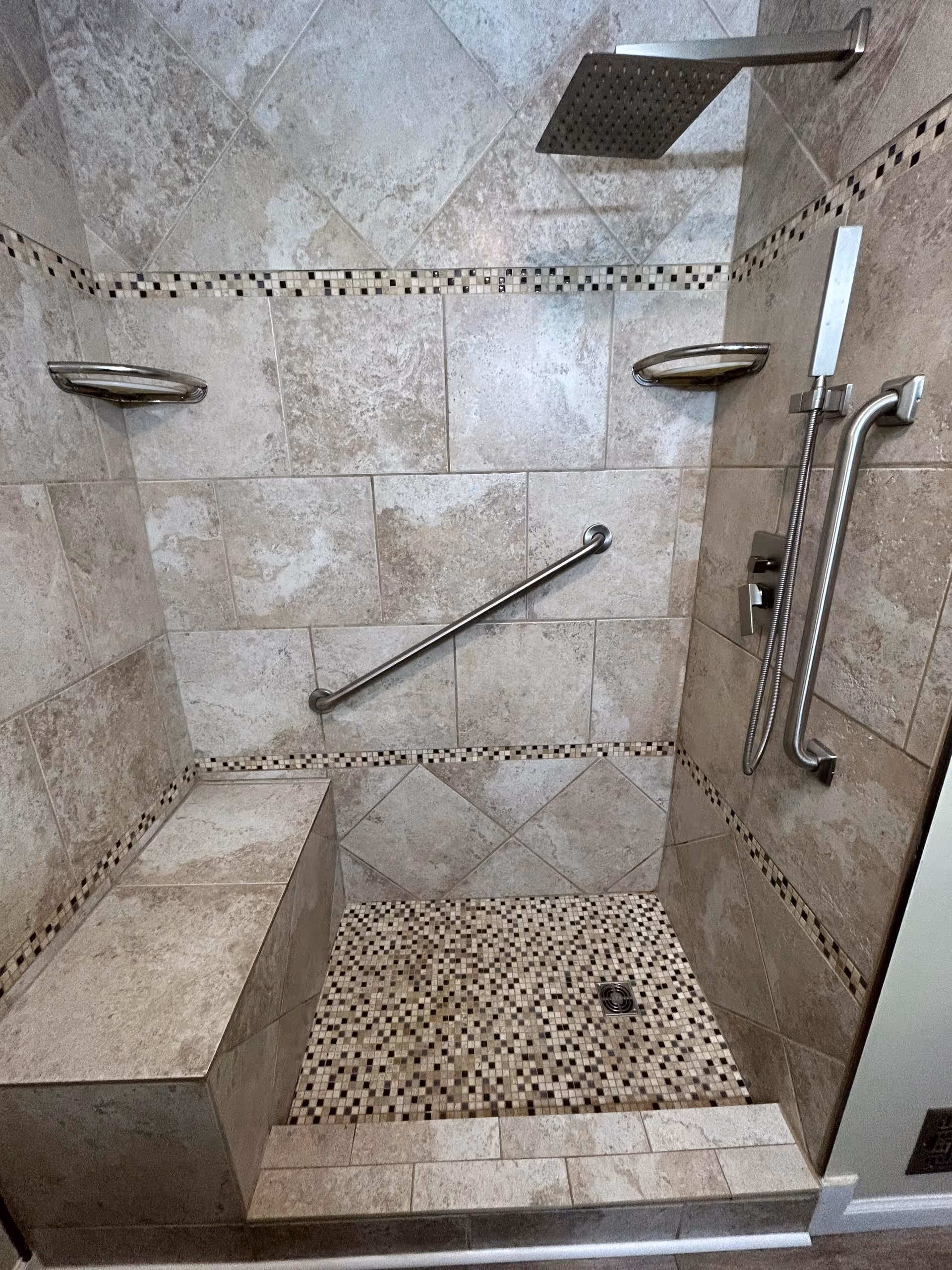 Tiled walk-in shower with a built-in bench, grab bars, a rain showerhead and a handheld sprayer.