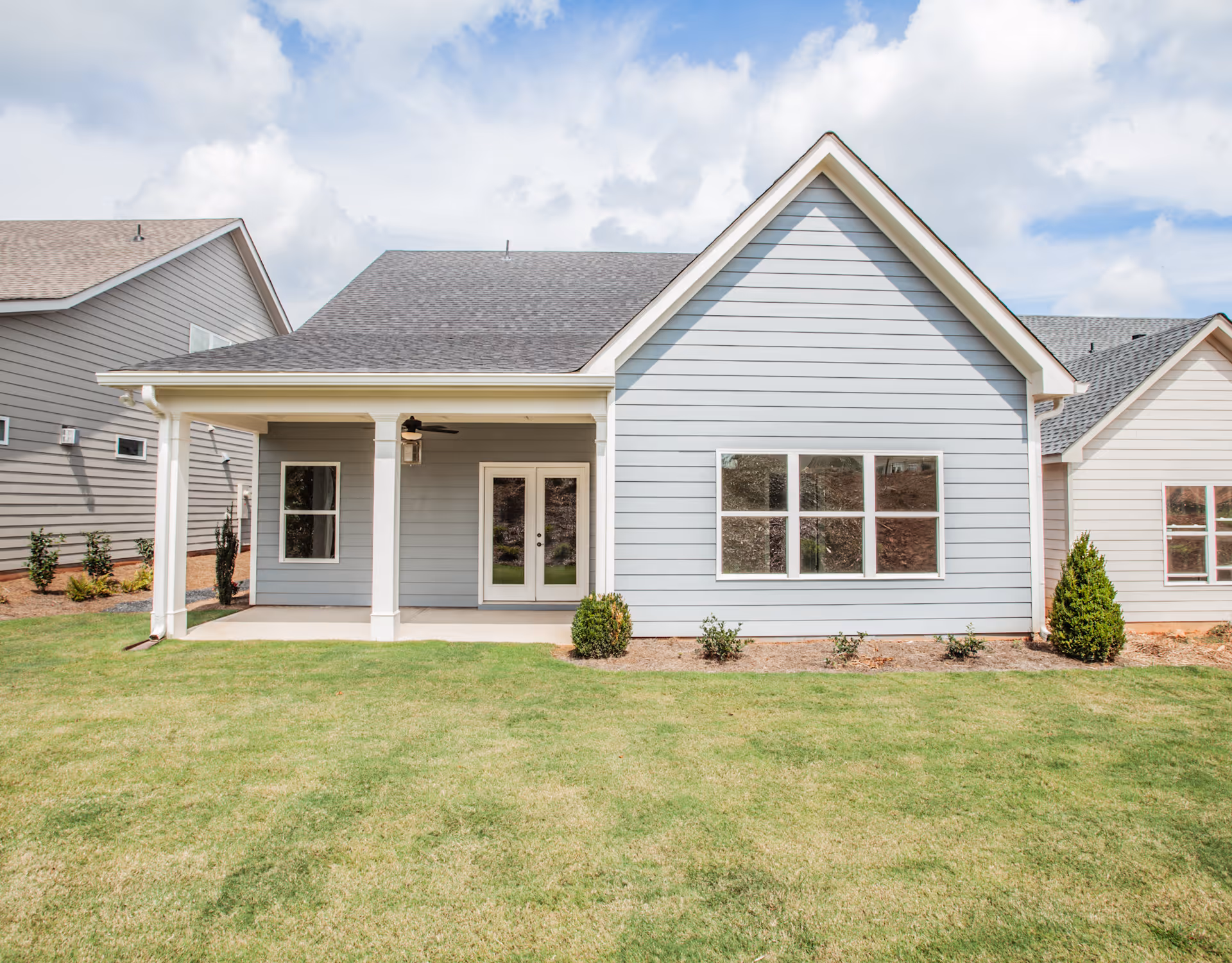 Light-blue single-story house exterior with a covered porch, double doors, large windows, and a grassy lawn.