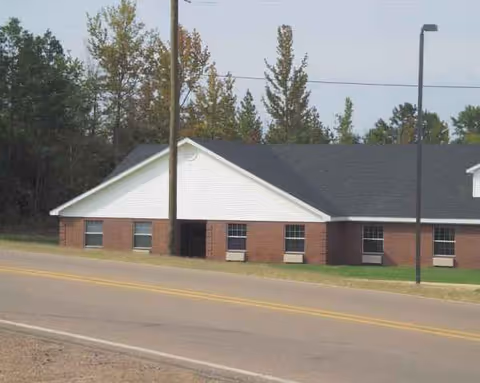 Exterior view of a single-story brick facility with a white gable roof beside a street.