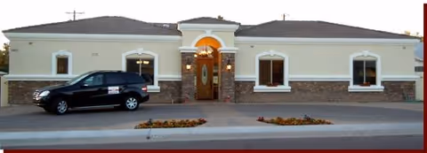 A single-story building with arched entrance, beige walls, stone base, and a parked black SUV.