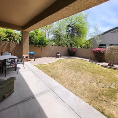Covered patio with seating overlooks a small grassy yard and trees.