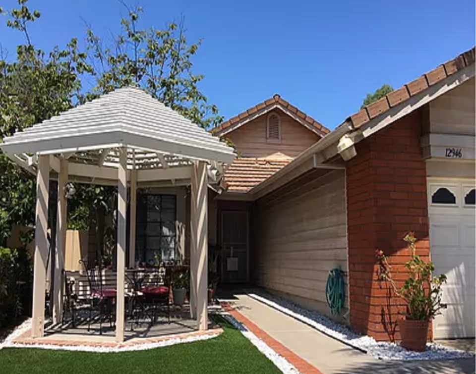 Outdoor seating under a gazebo in front of a single-story home.