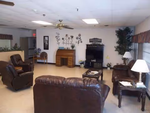 A spacious senior living lounge with leather seating, a fireplace, and a TV.