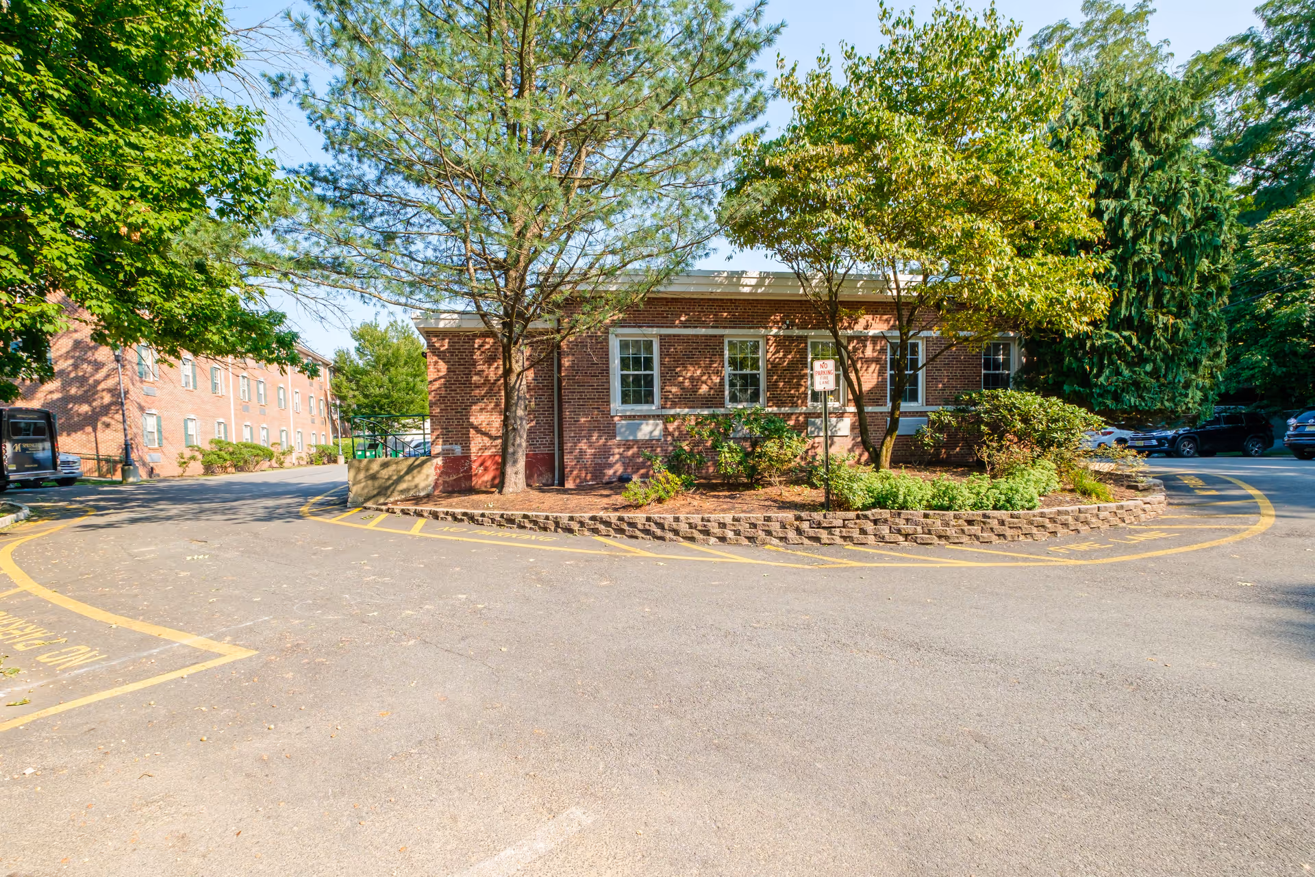 Brick single-story building surrounded by trees with a circular driveway and parking area in front.