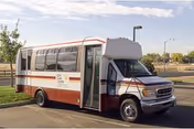 A small shuttle bus parked on a paved area near a grassy field with trees and a clear sky in the background. The bus has the name Life Care Center of Westminster on its side.