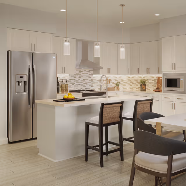 Modern kitchen with white cabinetry, a stainless steel refrigerator, a built-in microwave, a stove with a stainless steel hood, and a kitchen island with a sink and two bar stools. The backsplash features a mosaic tile design, and three pendant lights hang above the island. There is also a dining table with chairs visible in the foreground.