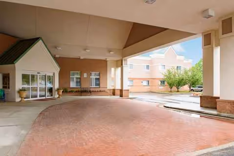 Covered entrance plaza of a senior living center with brick paving and plants.