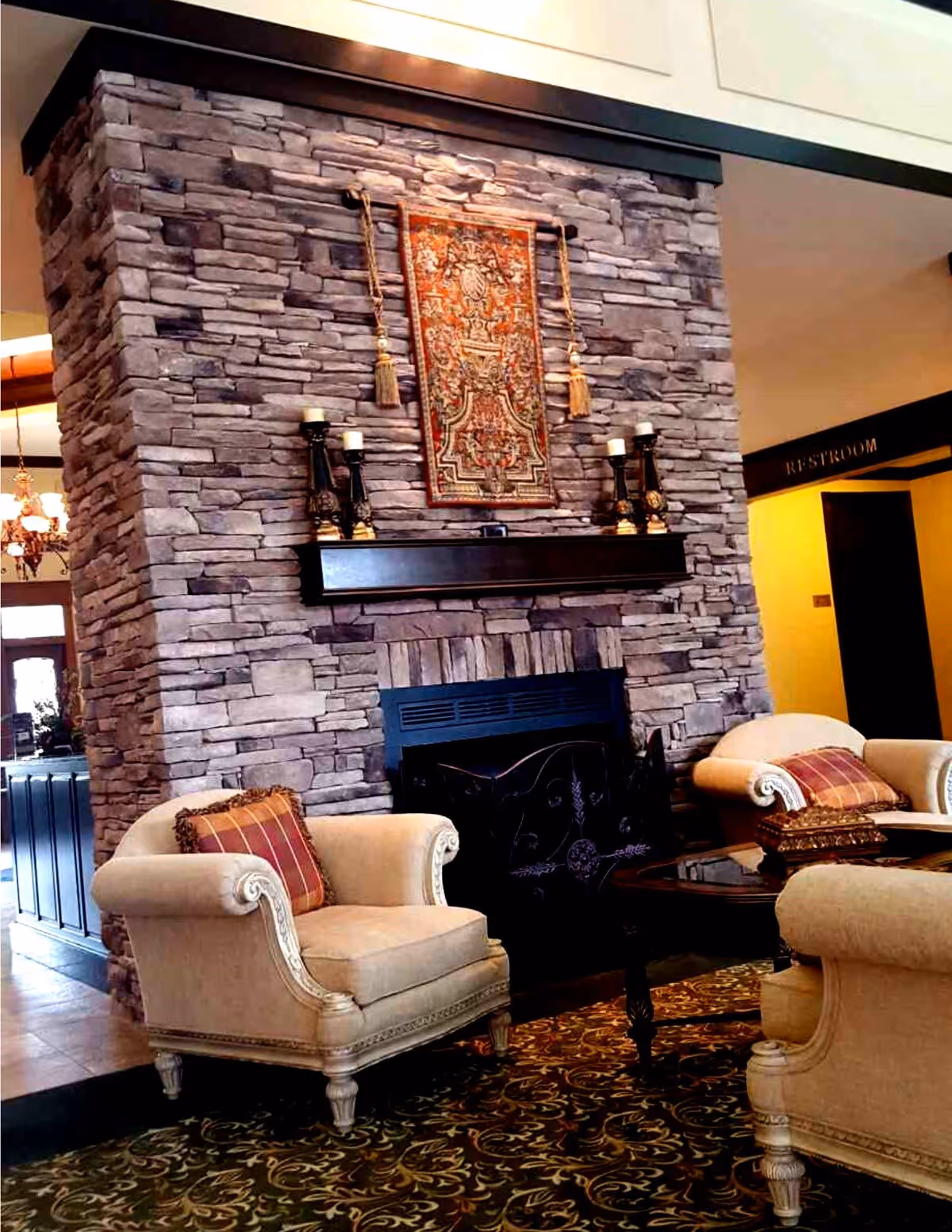 Interior seating area featuring a stone fireplace with a mantel, two upholstered armchairs and a coffee table.