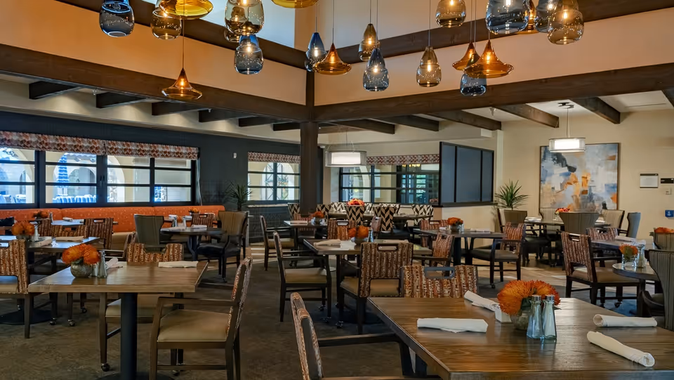 Spacious indoor dining room with multiple tables and chairs, hanging pendant lights, and floral centerpieces.