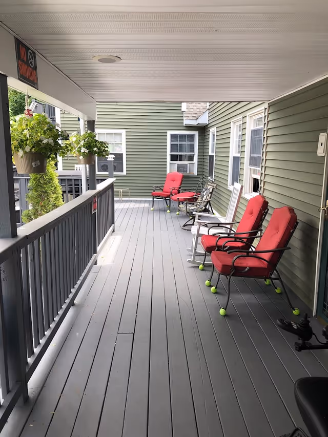 Covered exterior porch with gray decking and red-cushioned chairs along a green-sided building