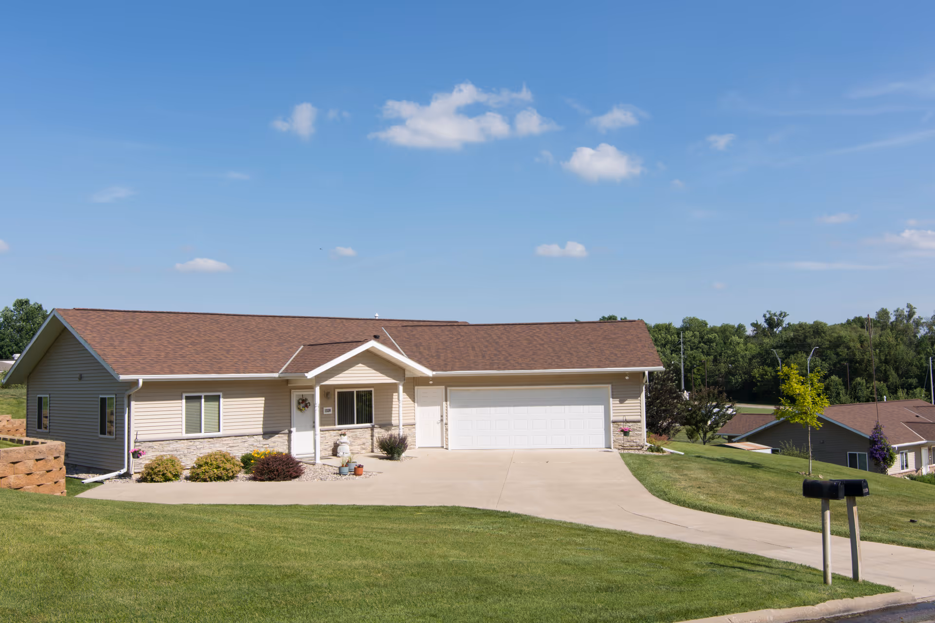 Single-story beige ranch-style house with an attached two-car garage and driveway on a grassy lot under a blue sky.