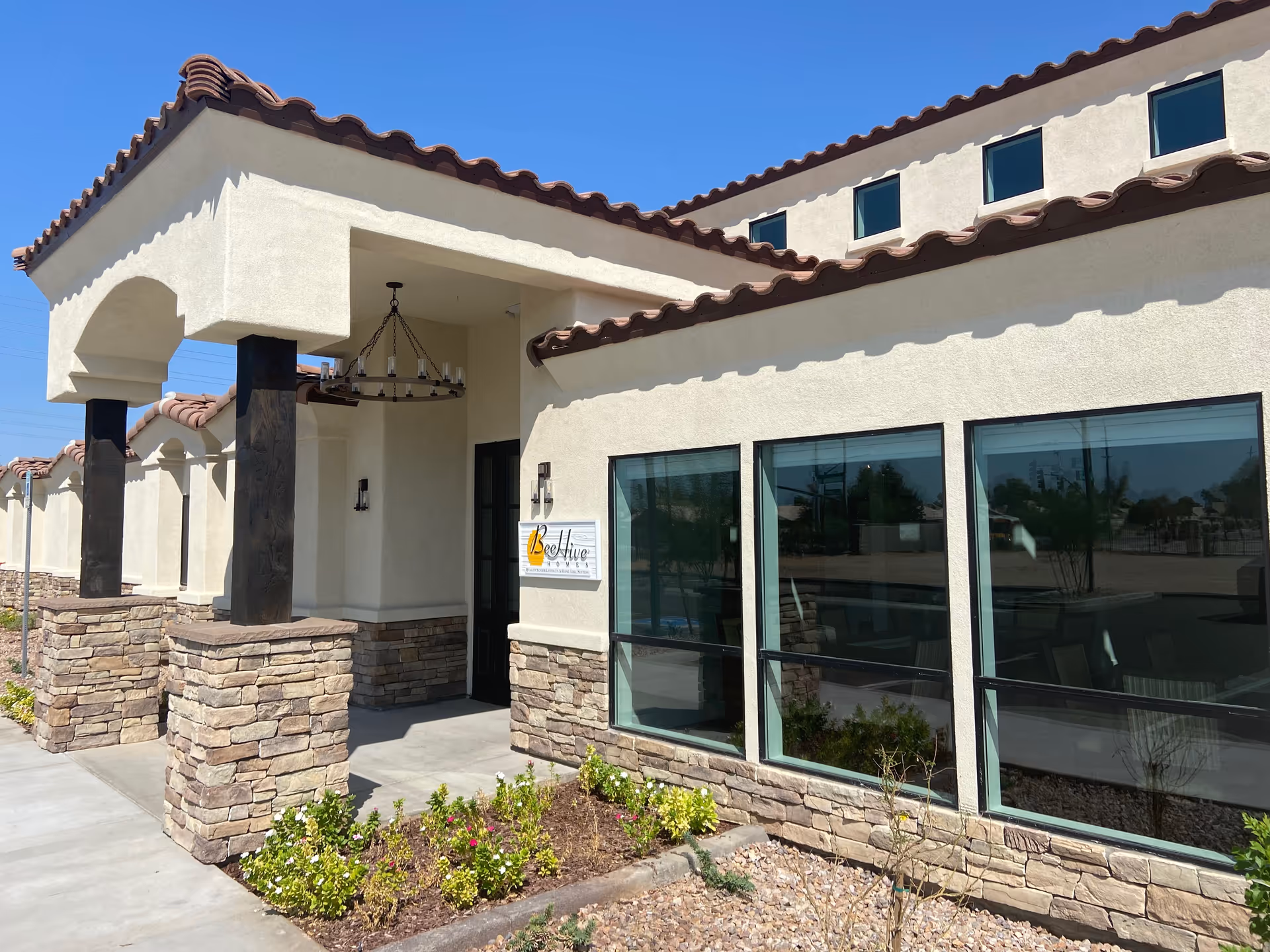 Front exterior of a BeeHive Homes assisted living building with stone columns, an arched covered entry and large windows.