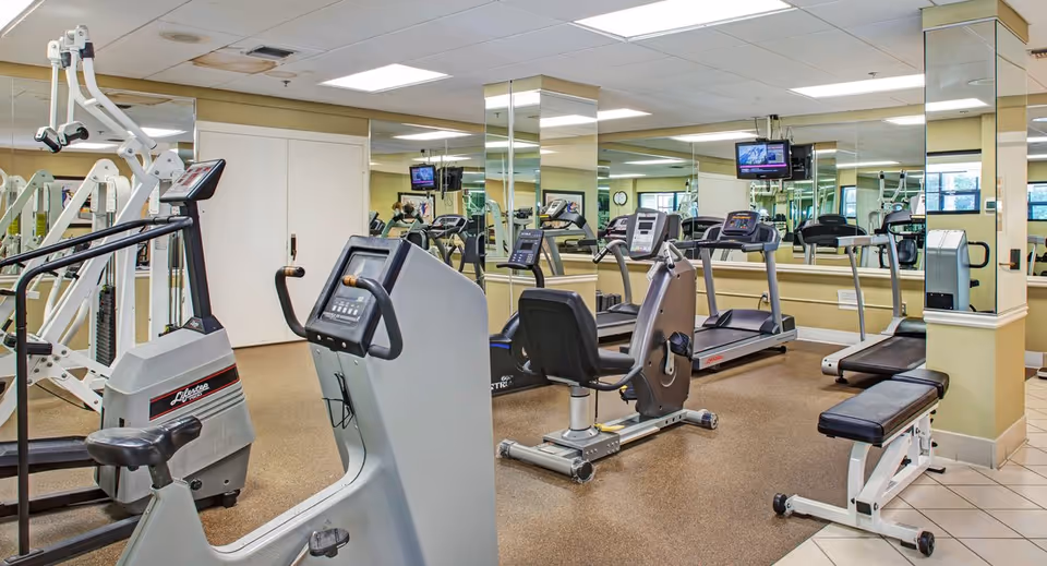 Fitness room with treadmills, stationary bikes, weight benches, mirrored walls, and mounted TVs.
