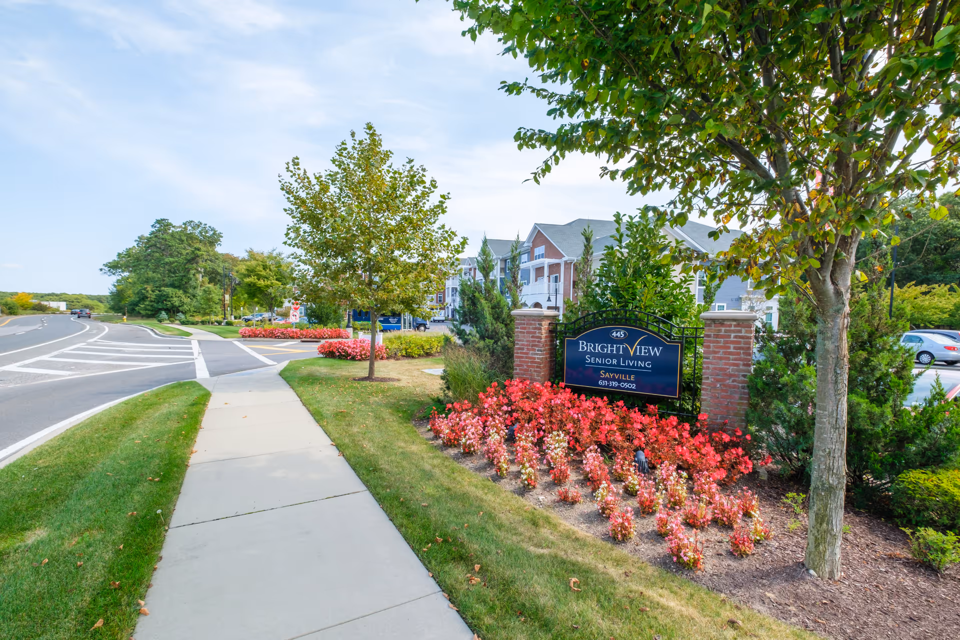 Sidewalk leading past a landscaped Brightview Senior Living sign with red flowers and the facility building in the background.