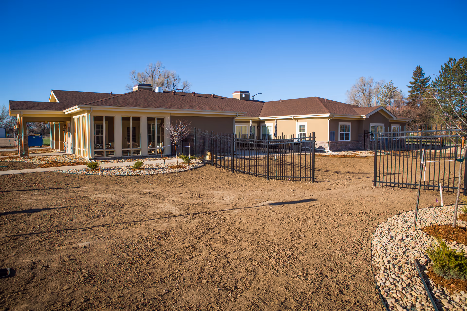 Single-story ranch-style building with a fenced courtyard, sparse landscaping, and a clear blue sky.