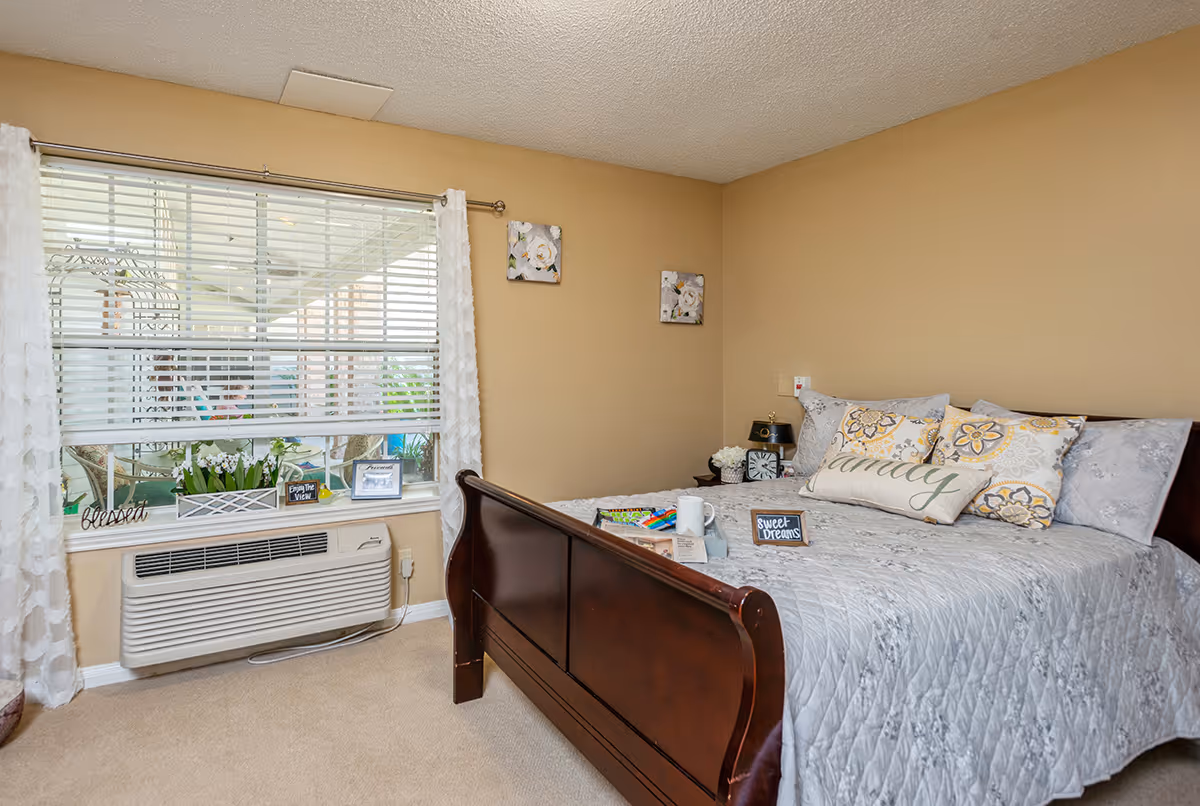 Cozy bedroom with a dark wooden sleigh bed, patterned pillows and a window with blinds and potted plants on the sill.