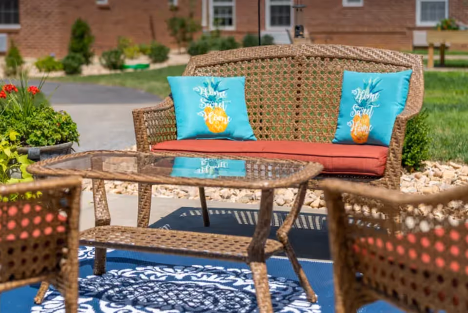 Wicker patio seating set with a glass-top table, red cushions and teal decorative pillows on an outdoor rug.