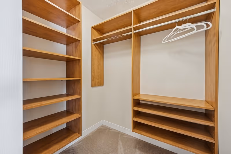 Empty walk-in closet with wooden shelves, hanging rods and a few white plastic hangers.