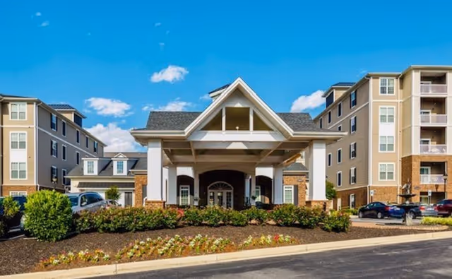 Front entrance of the Regency Crest senior living facility featuring a covered porte-cochere, landscaped flower beds, and multi-story wings.