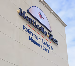 Exterior wall of a building with a sign that reads 'Monticello West Retirement Living & Memory Care' under a logo featuring a compass rose.