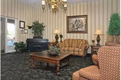 A cozy senior living lounge with sofas, armchairs, a coffee table, and artwork.