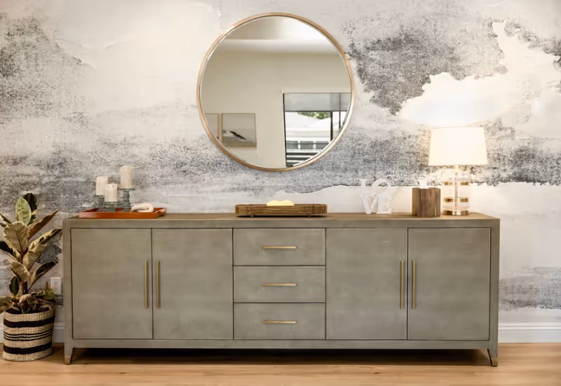 Modern sideboard with a round mirror, lamp, and decorative items against a textured wall.
