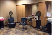 Interior salon area with styling chairs, hooded hair dryers, wash sinks, and wooden cabinetry.
