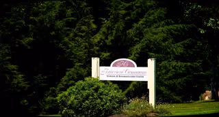 A front-area sign for Fairview Commons Nursing and Rehabilitation Center surrounded by trees.