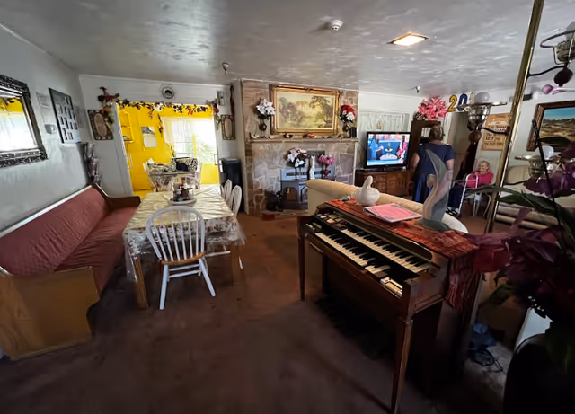 Cozy communal living room and dining area with a dining table, bench seating, an organ, fireplace, television, and floral decorations.