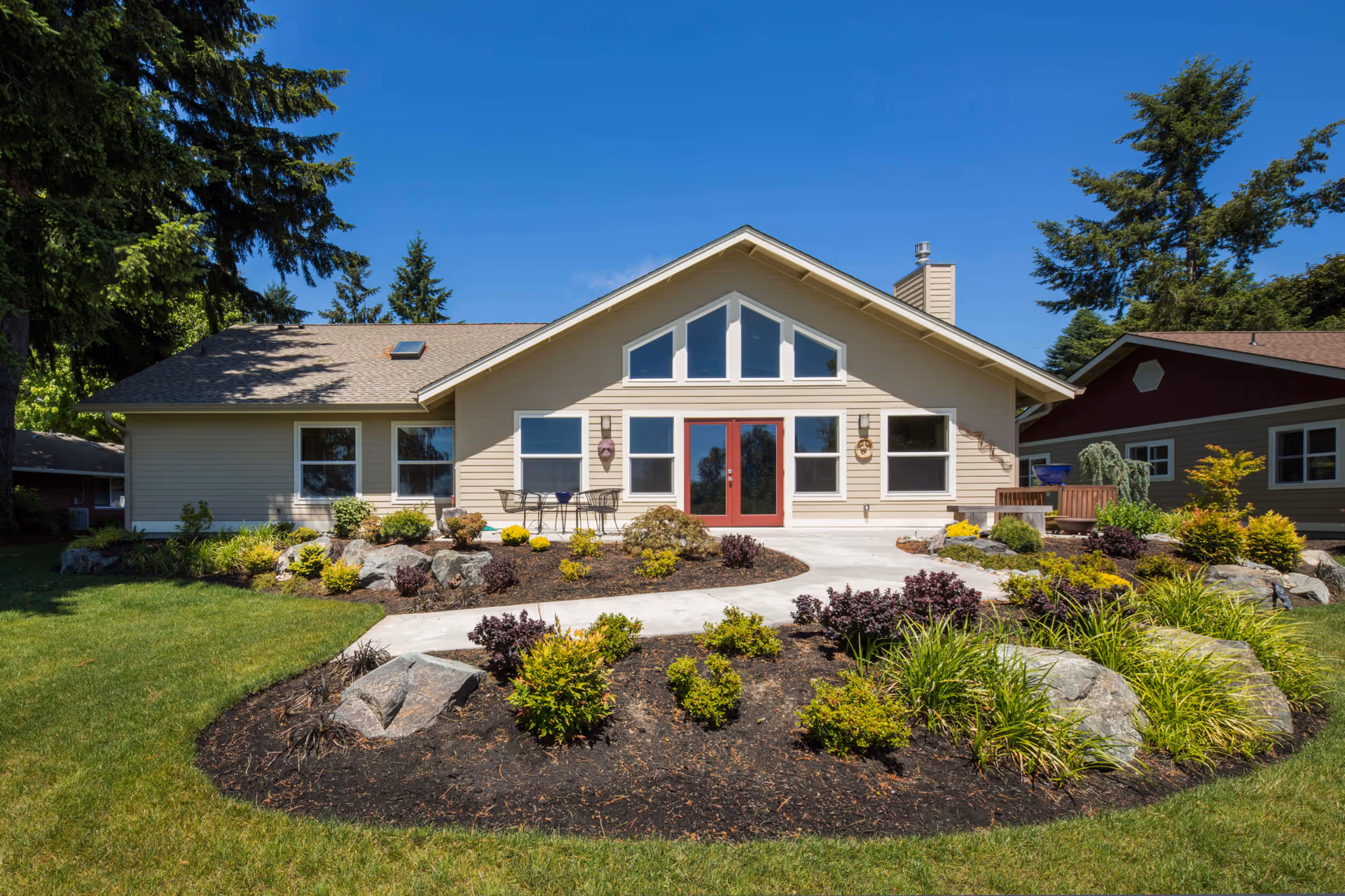 Front exterior of a single-story building with red double doors, large triangular windows, and landscaped grounds under a clear blue sky.